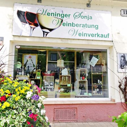 Fassade eines Weinladens namens Weininger Sonja. Der Laden ist auf Weinberatung und Verkauf spezialisiert. Im Schaufenster sind verschiedene Weinflaschen, Pflanzen und Blumen zu sehen.