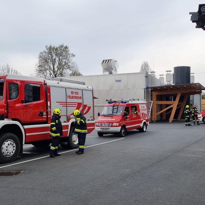 Ein roter Feuerwehrwagen und ein Rettungswagen sind auf der Straße geparkt, mit Feuerwehrleuten in Helmen.