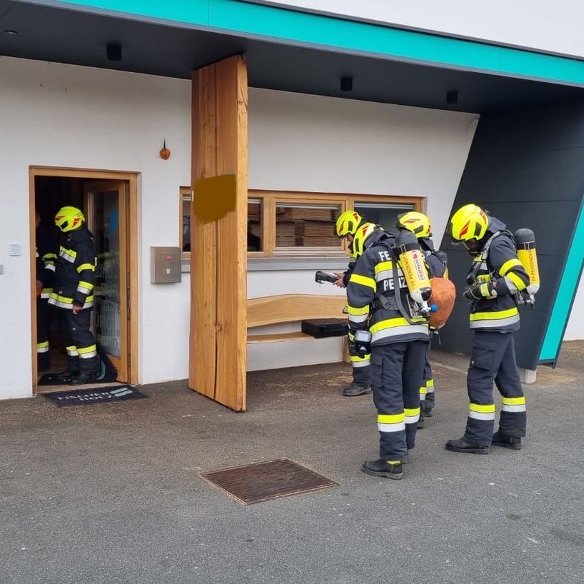 Fünf Feuerwehrleute mit gelben Helmen stehen vor einem Gebäude. Drei von ihnen tragen Sauerstoffflaschen und einen Feuerlöscher.