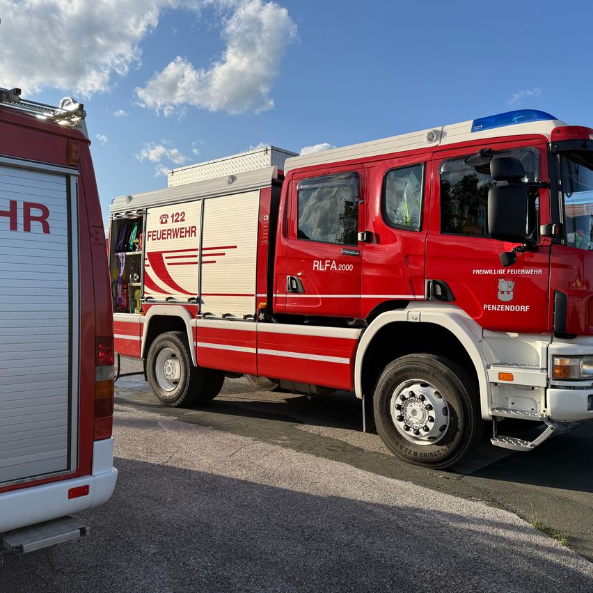 Ein roter Feuerwehrwagen mit der Nummer 122 ist am Straßenrand geparkt, mit einem Rückspiegel und Notleuchten auf dem Dach.