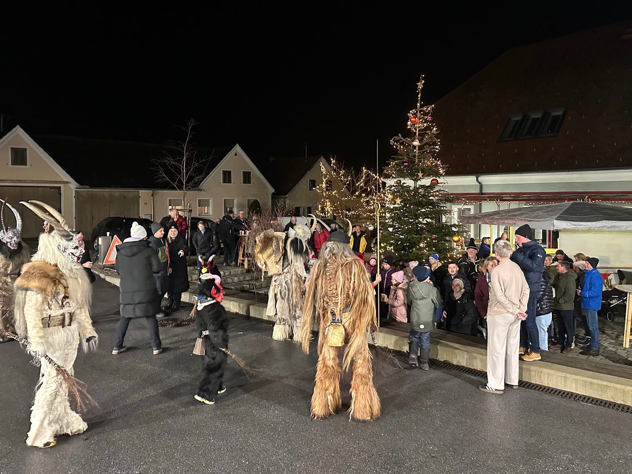 Ein nächtliches Treffen vor einem Weihnachtsbaum mit zwei Personen in pelzigen Kostümen. Viele Leute schauen zu.