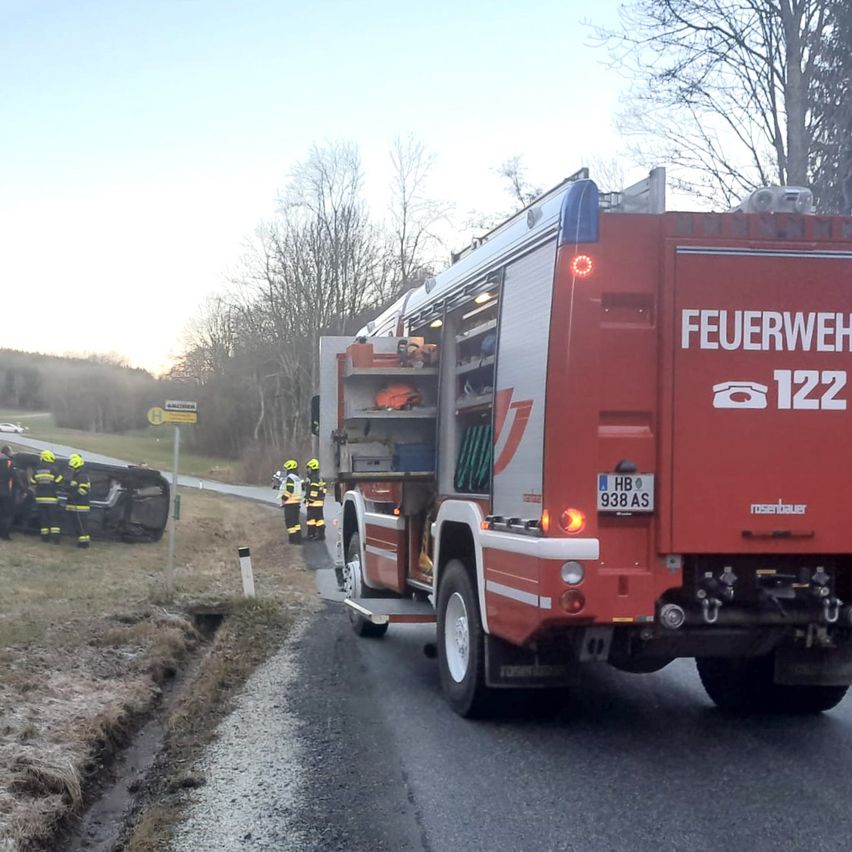 Ein Feuerwehrwagen mit der Nummer 122 ist am Straßenrand geparkt, Feuerwehrleute stehen um ein umgekipptes Auto.