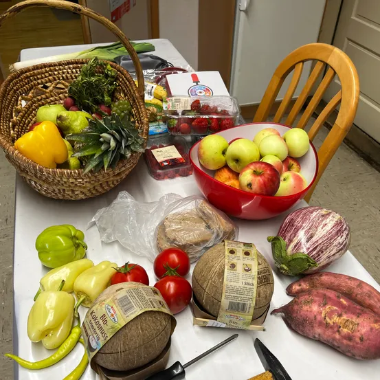 Ein Tisch mit einem Korb voller verschiedener Gemüsesorten, einem roten Apfelschüssel, einem Kokosnuss und anderen Früchten darauf.