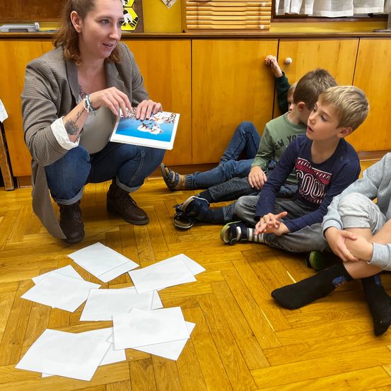 Eine Frau zeigt einem Kinderkreis ein Buch. Die Kinder sitzen um sie herum und schauen sich das Buch an.