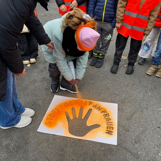 Eine Frau malt eine Hand mit den Worten Stopp Gewalt gegen Frauen auf ein weißes Poster.