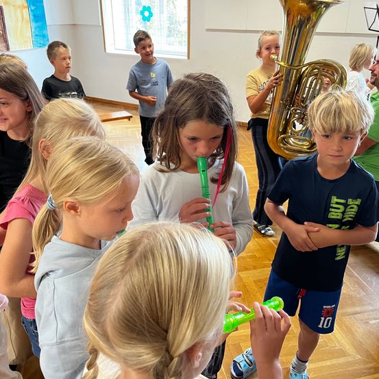 Kinder versammeln sich zum Spielen und Beobachten mit Instrumenten, eine Mädchen spielt eine Blockflöte.