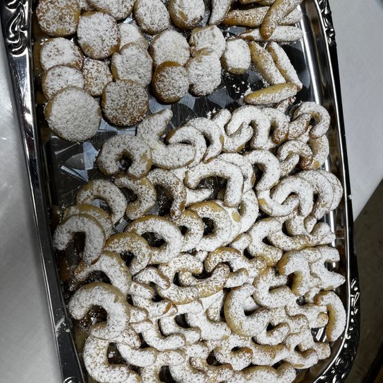 Ein silbernes Tablett gefüllt mit einer Vielzahl von mit Puderzucker überzogenen Desserts. Diese Leckereien sind in einem Haufen angeordnet und haben die Form von Donuts und Brezeln.