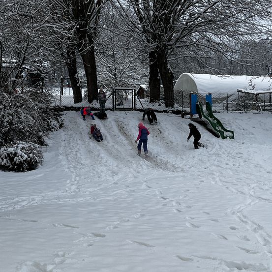 Eine Gruppe von Kindern spielt im Schnee. Sie rutschen eine Schneerutsche hinunter.