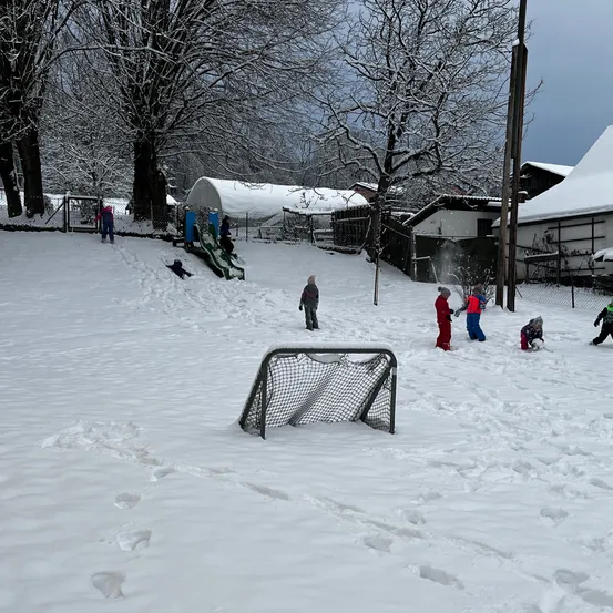 Mehrere Kinder spielen im Schnee, einige rutschen einen schneebedeckten Hang hinunter und andere spielen mit einem Hockeynetz.