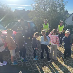Eine Gruppe von Kindern steht im Kreis mit zwei Polizeibeamten in gelben Westen.