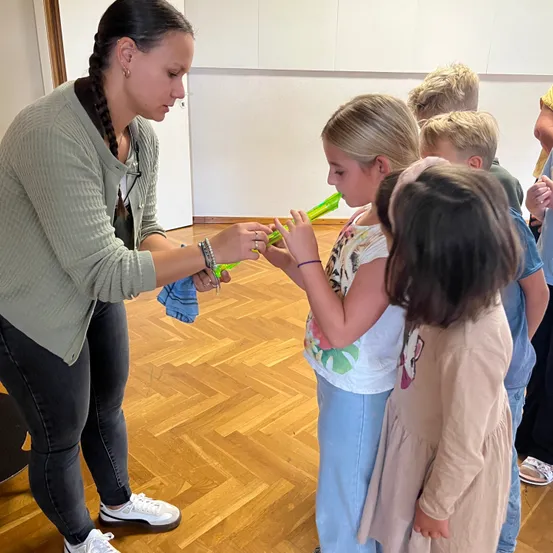 Eine Frau zeigt einer Gruppe von Kindern, wie man grüne Plastikpfeifen benutzt.