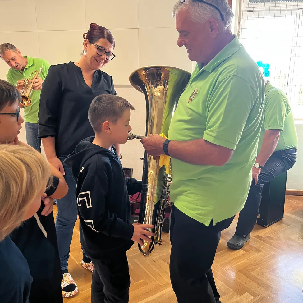 Ein junger Junge spielt Tuba, während ein erwachsener Mann in einem grünen Shirt zusieht.