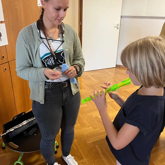 Eine Frau bringt einem jungen Mädchen das Spielen einer grünen Flöte bei.