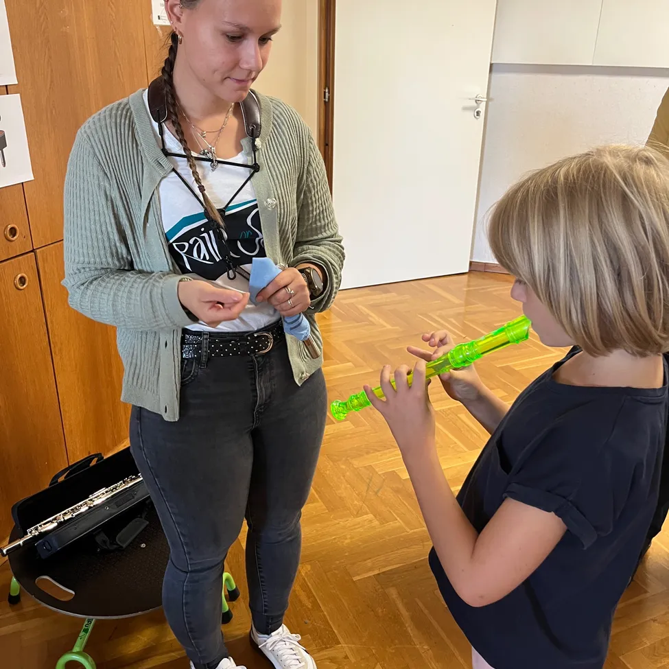 Eine Frau bringt einem jungen Mädchen das Spielen einer grünen Flöte bei.