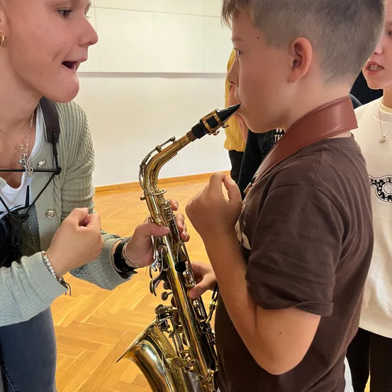 Eine Frau bringt einem Jungen das Spielen der Saxophon in einem Raum mit Holzböden bei.