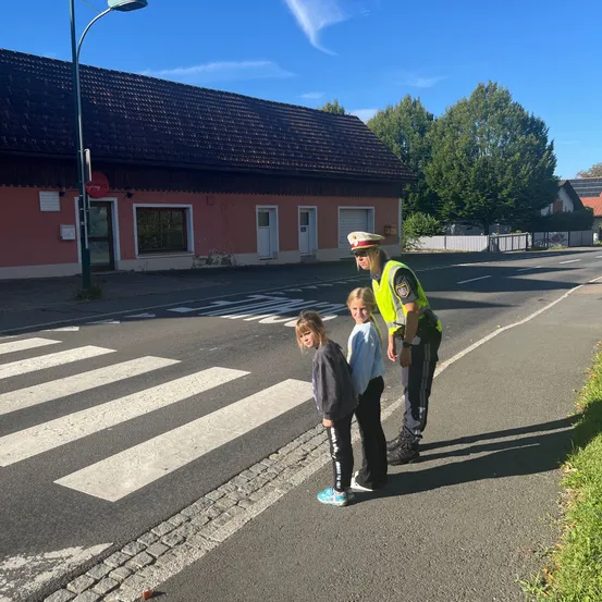 Eine Verkehrspolizistin hilft zwei jungen Mädchen beim Überqueren der Straße an einem Zebrastreifen.