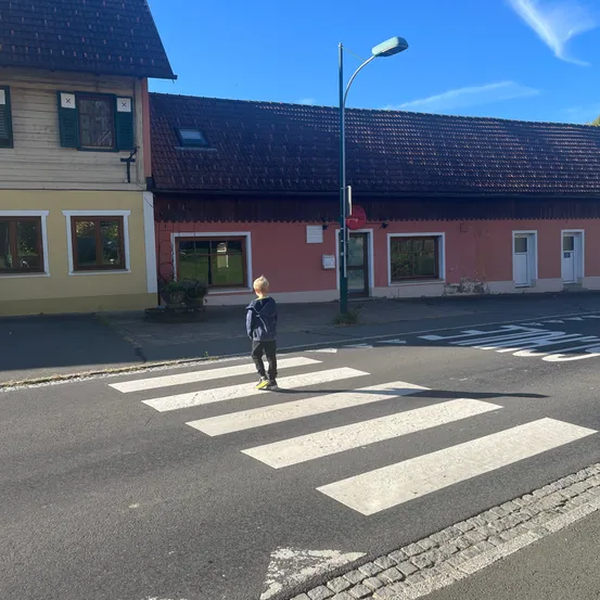 Ein junger Junge steht auf einem Zebrastreifen vor einem Gebäude mit rotem Dach.
