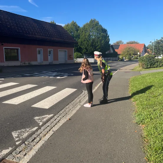 Ein Polizist spricht mit einem jungen Mädchen auf dem Bürgersteig in der Nähe eines Zebrastreifens.