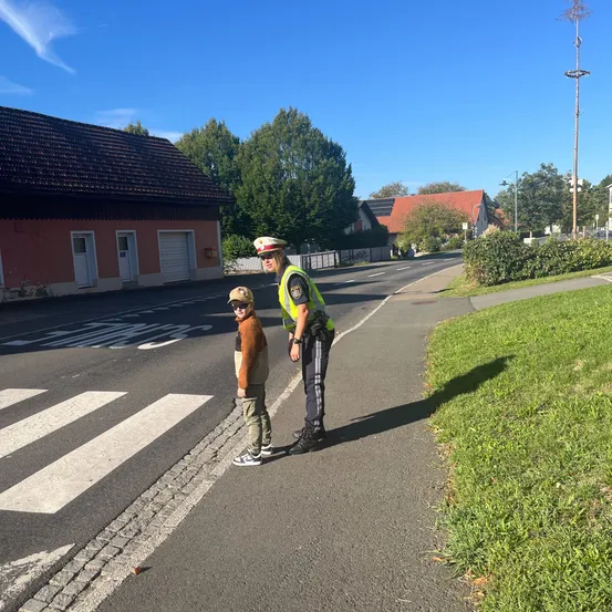 Ein Polizist steht auf dem Bürgersteig neben einem Kind an einer Fußgängerampel.