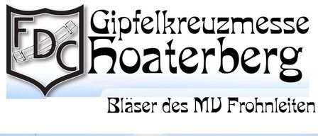 Eine Gruppe von Menschen, möglicherweise Pilger, geht in einem Grasbereich. Ein Kreuz ist auf der linken Seite. Viele Menschen sitzen auf dem Gras und einige stehen. Eine große Gruppe von Menschen ist auf dem Berg.