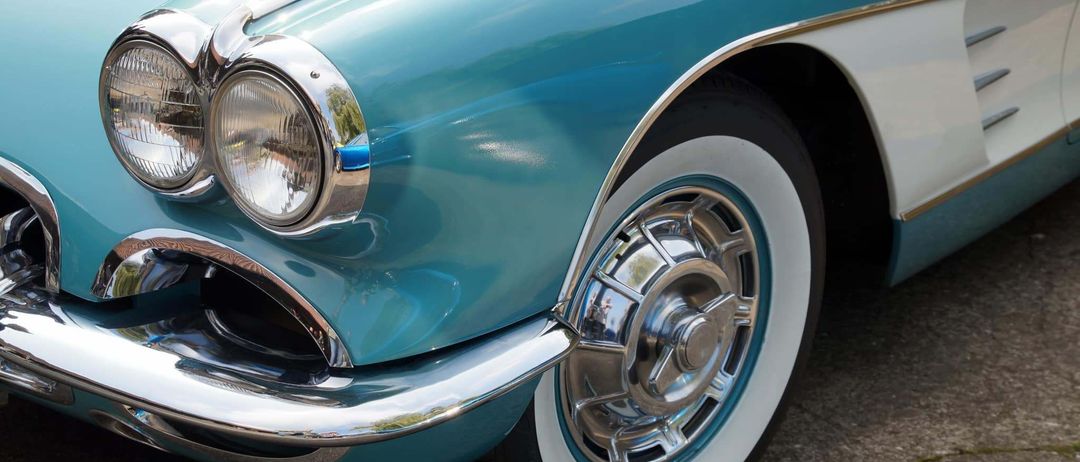 Nahaufnahme eines klassischen blauen Autos mit Chrom-Akzenten, mit polierter silberner Radkappe und Weißwandreifen.