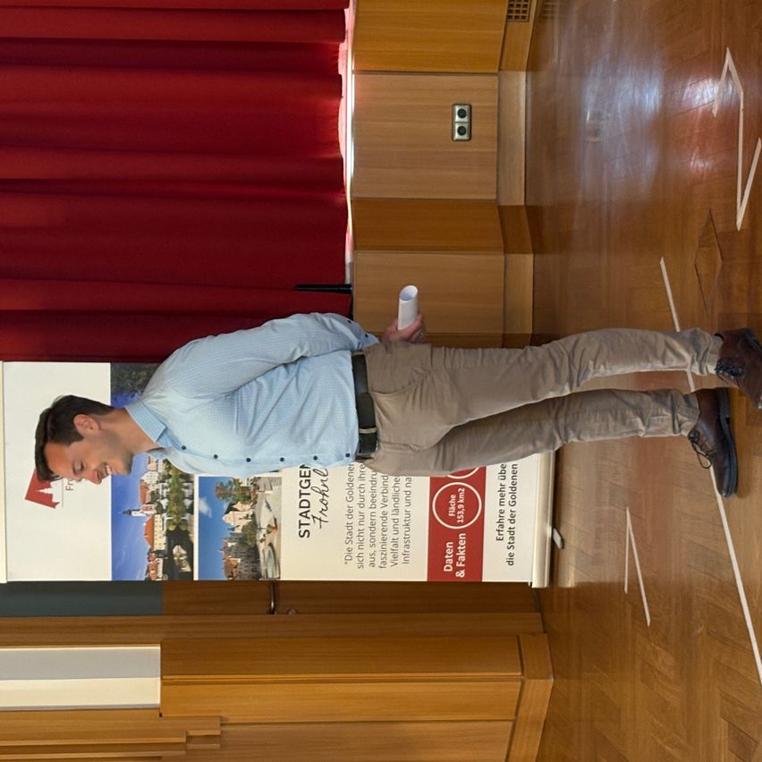 Ein Mann, der neben einem Werbeplakat steht und eine Rolle weißes Papier hält, drinnen.