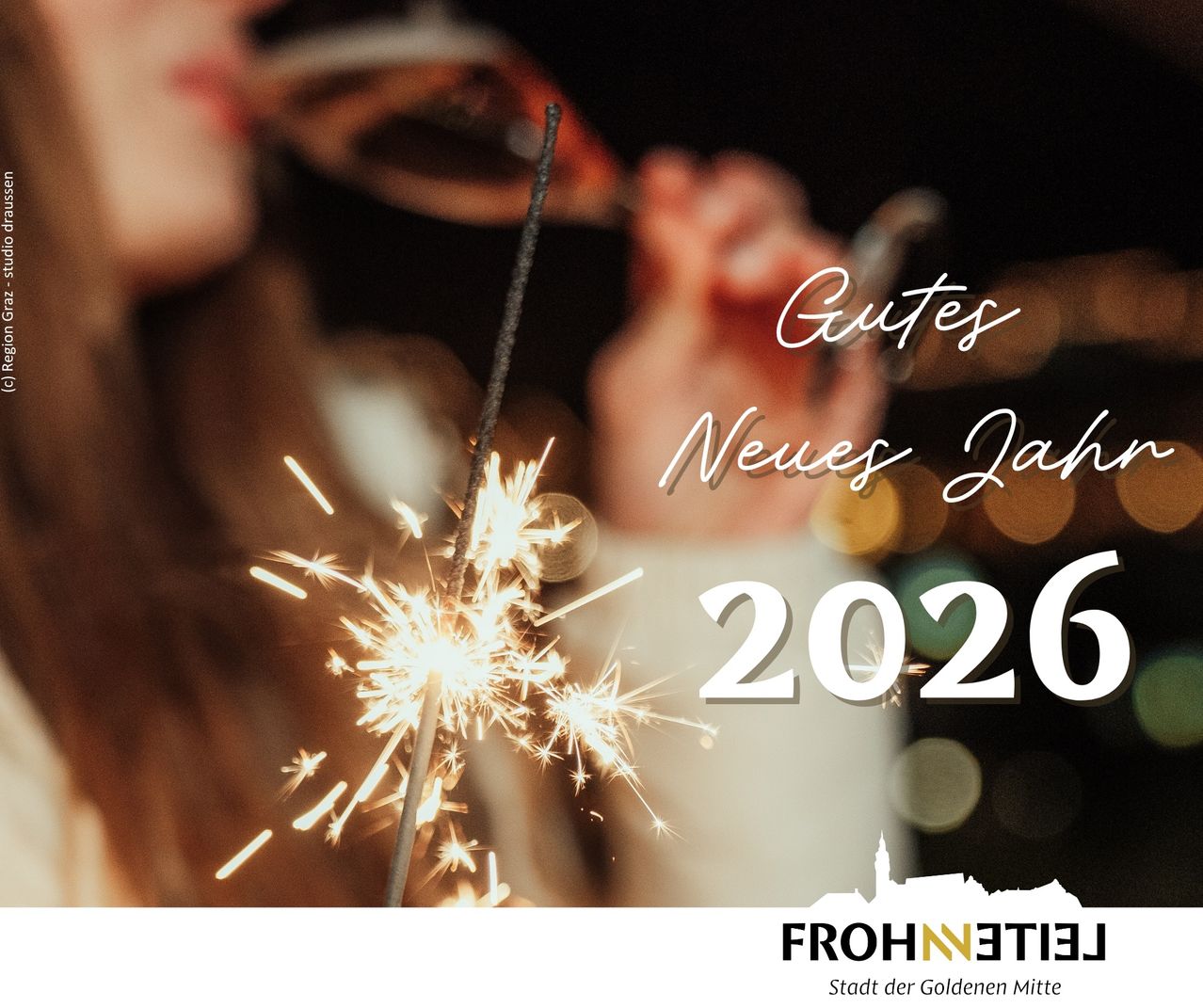 Eine Person trinkt aus einem Glas mit Feuerwerk und den Worten 'Gutes Neues Jahr 2026' im Vordergrund. Der Hintergrund ist unscharf.