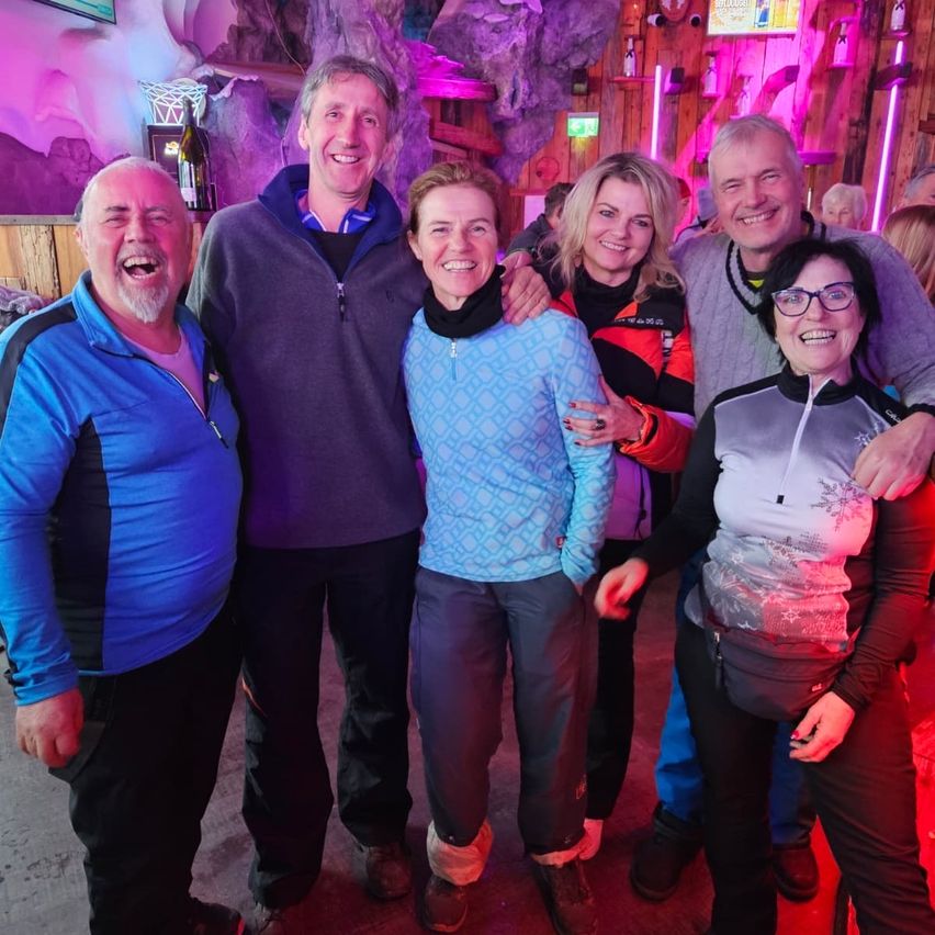 Eine Gruppe lächelnder Erwachsener steht zusammen in einem farbenfrohen, beleuchteten Raum, wahrscheinlich auf einer Party oder einem Event.