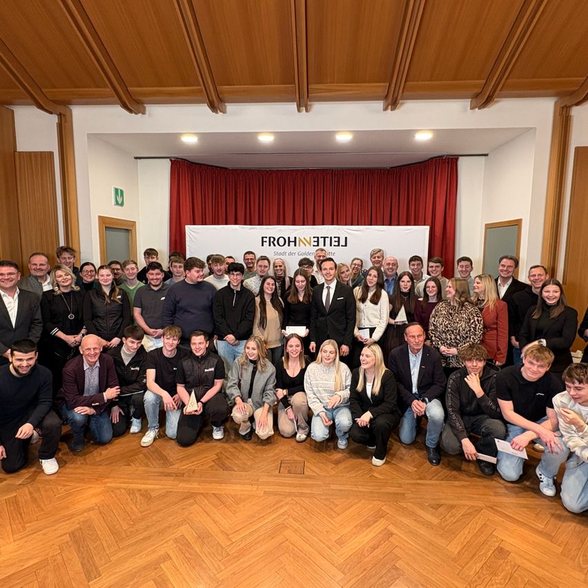 Eine Gruppe von Menschen in formeller Kleidung versammelt sich für ein Foto vor einem Banner mit den Worten Frohne Leitz.