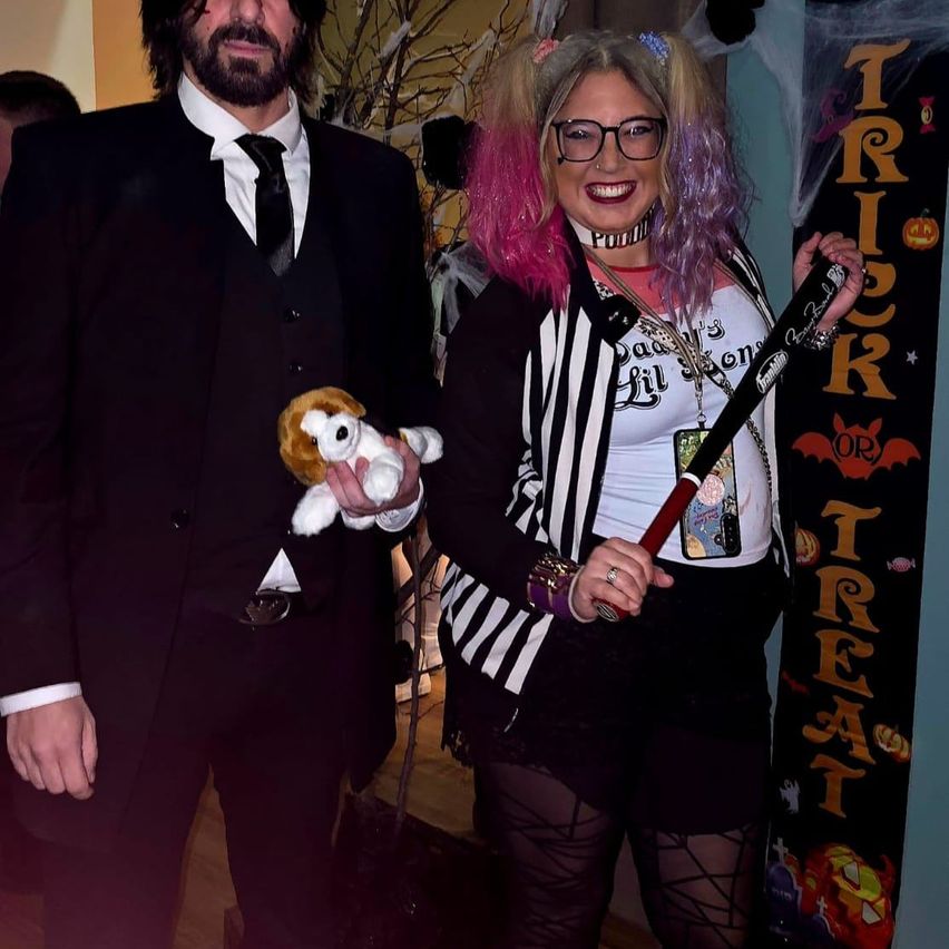 Ein Mann und eine Frau in Halloween-Kostümen. Der Mann hält ein Plüschtier und die Frau hat eine Fledermaus.