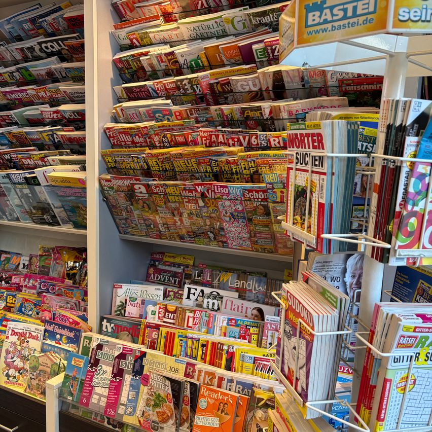 A store filled with numerous magazines and books on display, organized on shelves and racks, some featuring colorful covers and illustrations.