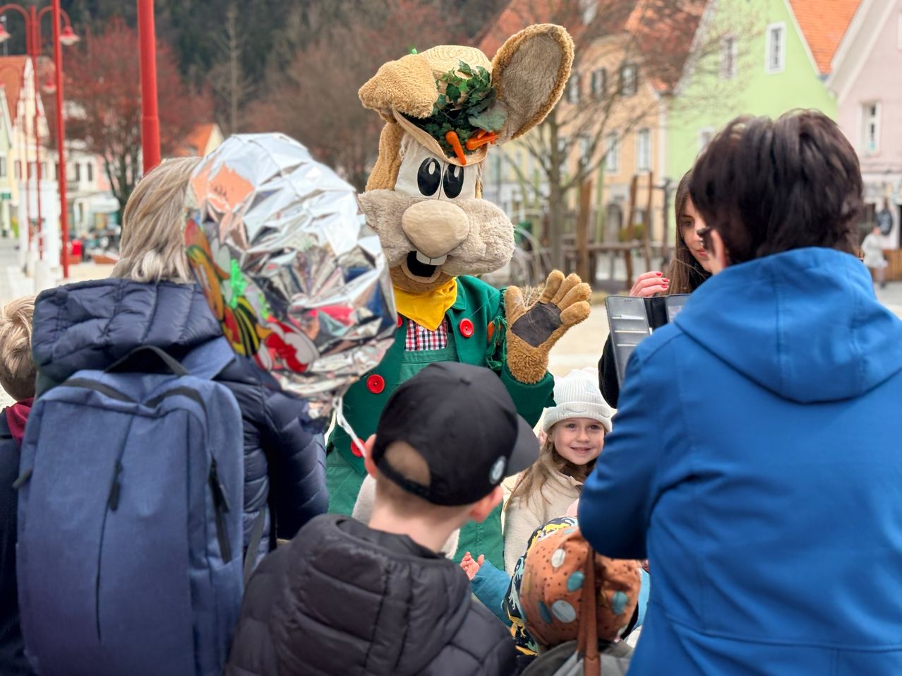 Ein Maskottchen in einem Hasenkostüm begrüßt eine Gruppe von Kindern und Erwachsenen in einem Park.
