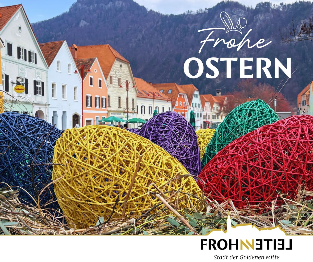 Ein farbenfrohes Display von Ostereiern wird vor einem Dorf mit traditionellen Häusern und Bergen im Hintergrund gezeigt.
