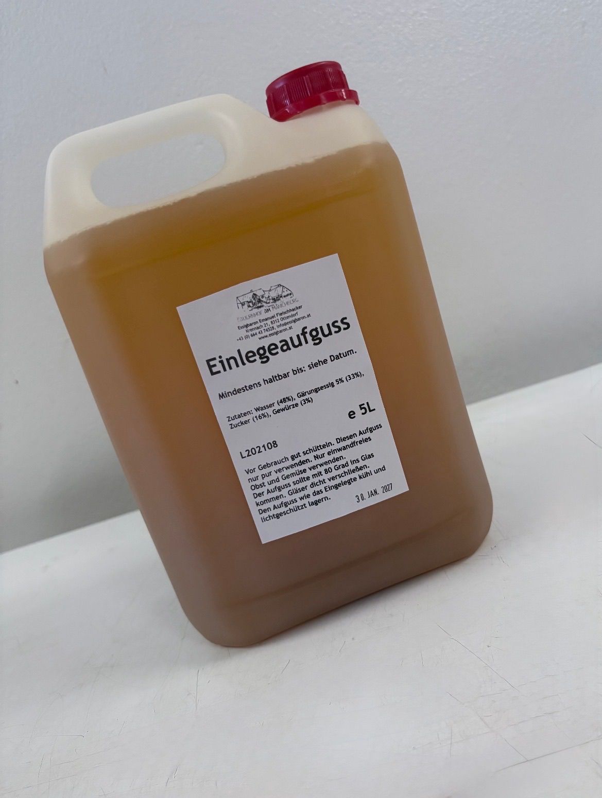 A large bottle of Einlegeaufguss, a liquid product with a label indicating it contains water, sugar, and gelatin. The bottle is filled to the brim and has a red cap.