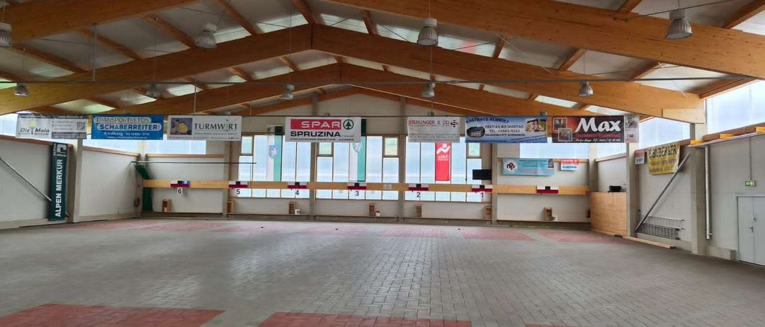 Ein überdachter Schießstand mit Holzdach und großen Fenstern. Banner sind über den Fenstern angebracht. Der Boden hat rote und weiße Markierungen.