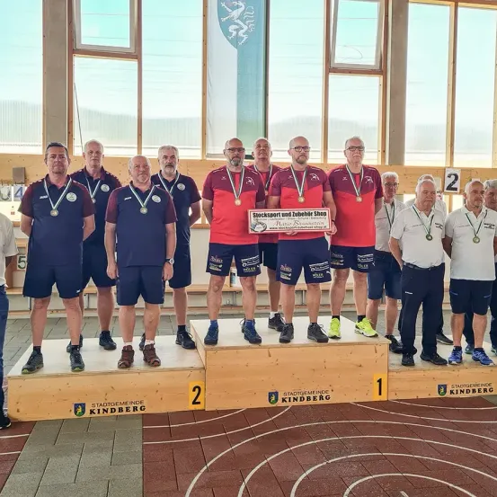 Eine Gruppe von Männern steht mit Medaillen auf einem Podest, trägt blaue und rote Sportuniformen. Sie halten ein Zertifikat für Stocksport und Zubehör Shop. Die Umgebung scheint ein Sportereignis zu sein.