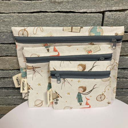 Drei gezippte Taschen mit Weltraumthema liegen auf einer weißen Oberfläche. Die größte Tasche hat eine Erdkugel und andere Gegenstände, die mittlere zeigt ein Teleskop und die kleinste zeigt ein Mädchen mit einem Fuchs.