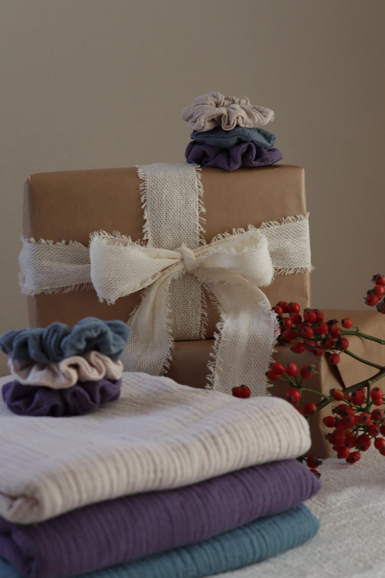 Verpackte Geschenke mit Jutebändern und Schleifen, gekrönt von farbenfrohen Stoffhaargummis, neben einer Traube roter Beeren.