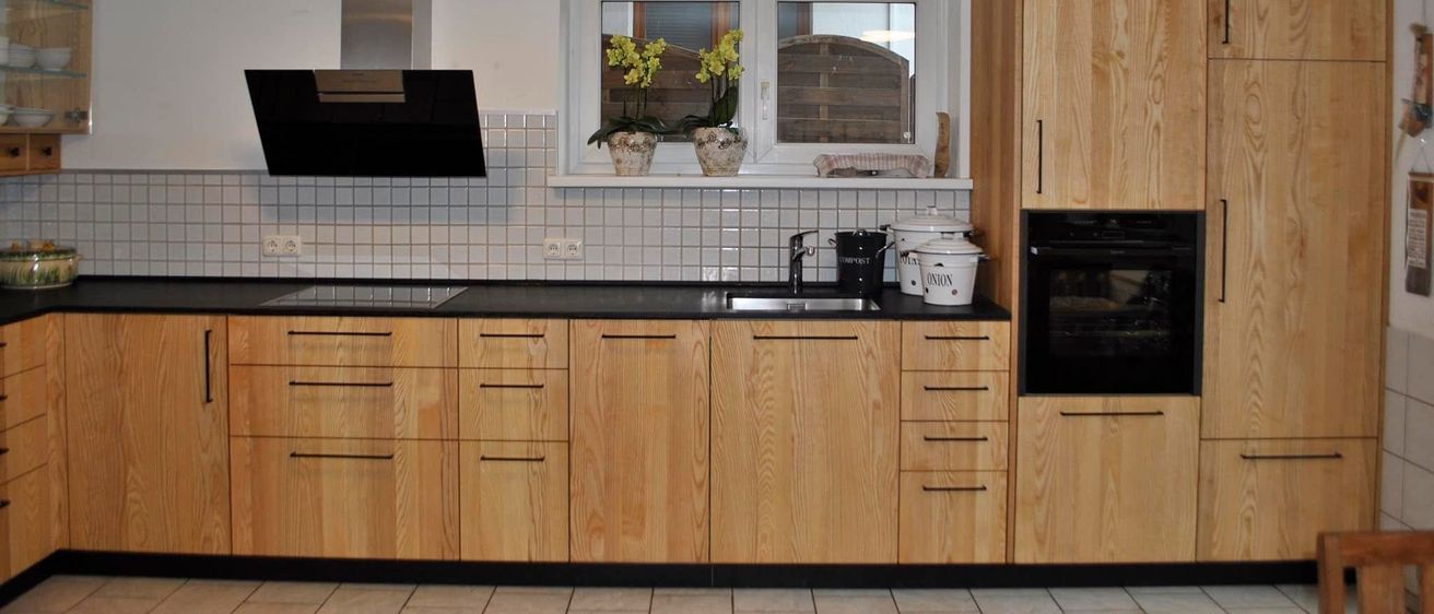 Eine Küche mit Holzschrank und Arbeitsplatte, einer Spüle mit Wasserhahn, einem Herd und einem Fenster mit Blumenvasen auf der Fensterbank.