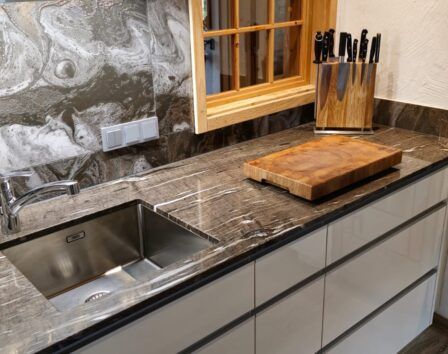 Eine moderne Küche mit Marmorarbeitsplatte, Edelstahlgeräten, einem Waschbecken mit Wasserhahn und einem Holzschneidebrett mit Messern.