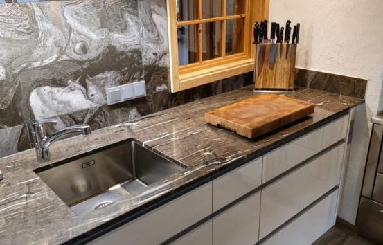 Eine moderne Küche mit Marmorarbeitsplatte, Edelstahlgeräten, einem Waschbecken mit Wasserhahn und einem Holzschneidebrett mit Messern.