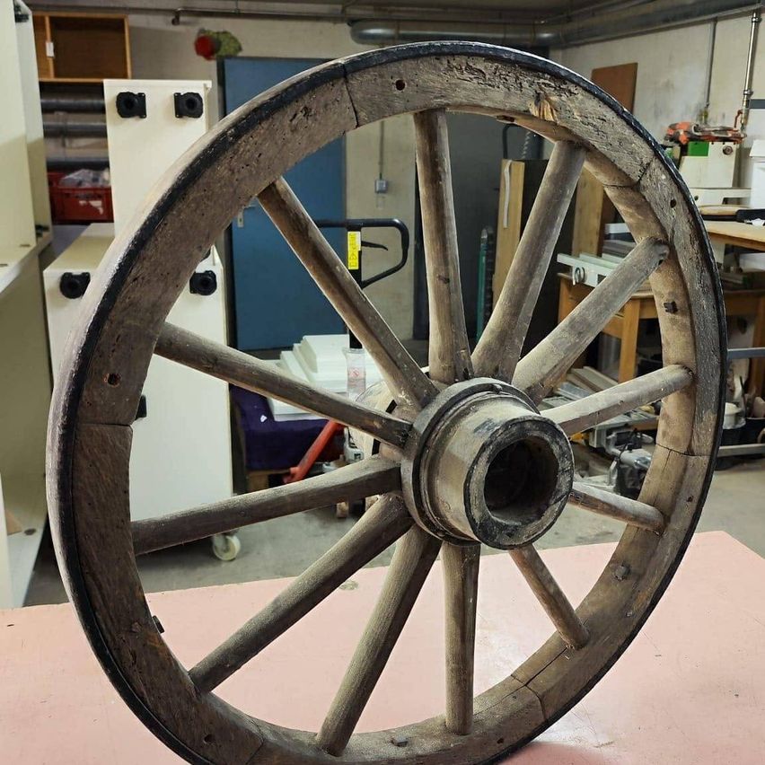 Ein altes Holzrad mit einem Metallring wird in einer Werkstatt auf einer rosa Oberfläche ausgestellt.