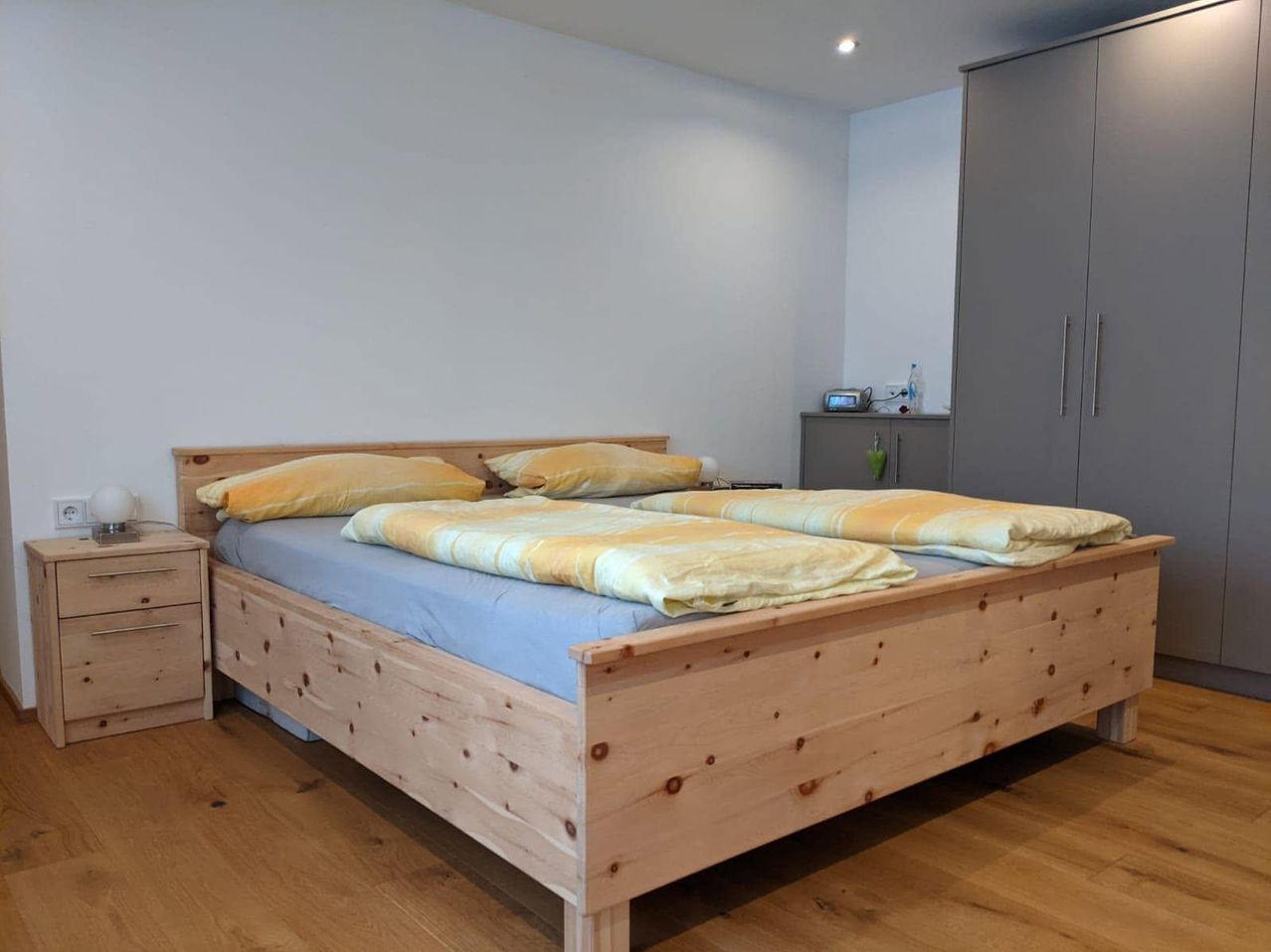 Ein Holzbett mit blauen Laken und zwei gelben Kissen in einem Schlafzimmer mit weißen Wänden und Holzboden.