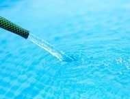 Ein Nahaufnahme eines schwarzen Schlauchs, der Wasser in einen Swimmingpool leitet und einen sanften Strom erzeugt. Das Wasser ist klar und blau.