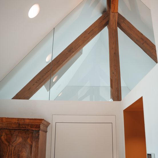 Ein Raum mit Holzbindern und Glasscheiben. Die Glasscheiben reflektieren das Licht von der Decke. Der Raum hat einen Holzschrank auf der linken Seite.