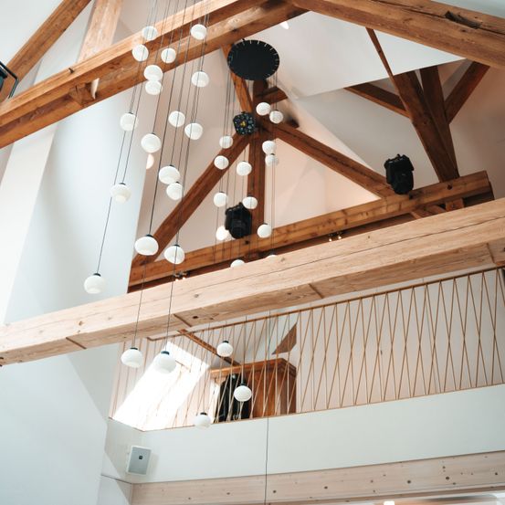 Ein Raum mit Holzbalken, einem Holzbalkon und hängenden Lampen. Der Raum hat ein schlichtes und elegantes Design.