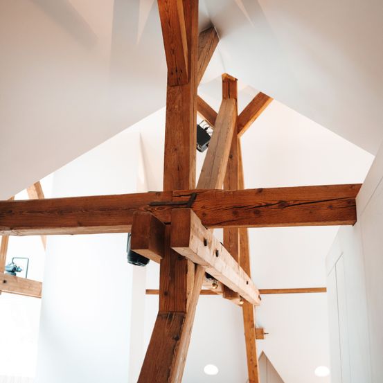 Ein Nahaufnahme von Holzbalken, die eine dreieckige Struktur an einer weißen Decke bilden.