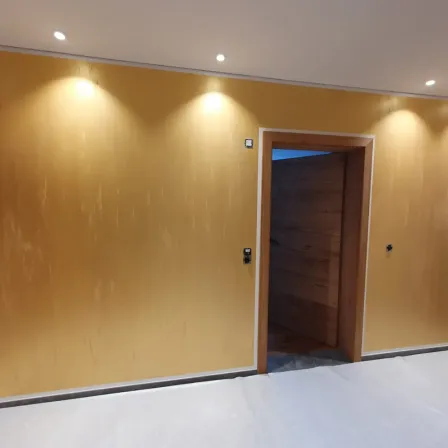 Ein leerer Raum mit gelber Wand und Holztür. Die Wand hat eine glänzende Oberfläche. Es gibt Lichter an der Decke.