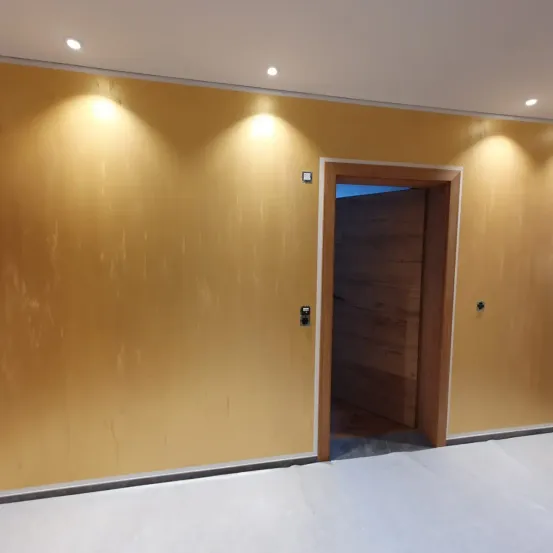 Ein leerer Raum mit gelber Wand und Holztür. Die Wand hat eine glänzende Oberfläche. Es gibt Lichter an der Decke.