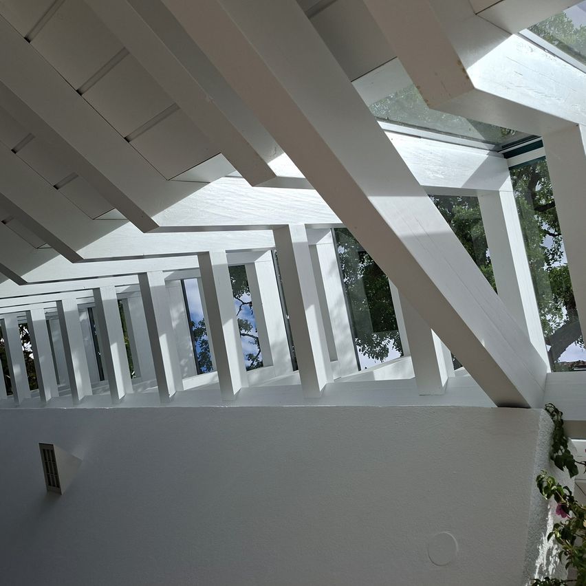 Ein modernes architektonisches Design mit weißen Holzbalken und Glasfenstern, das natürliches Licht in den Raum lässt.